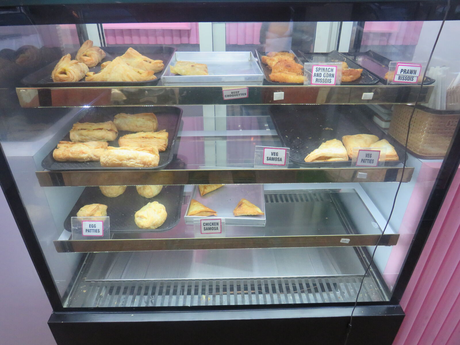Inviting bakery display showing fresh savory snacks including samosas, patties, croquettes and rissois in Panjim Goa location